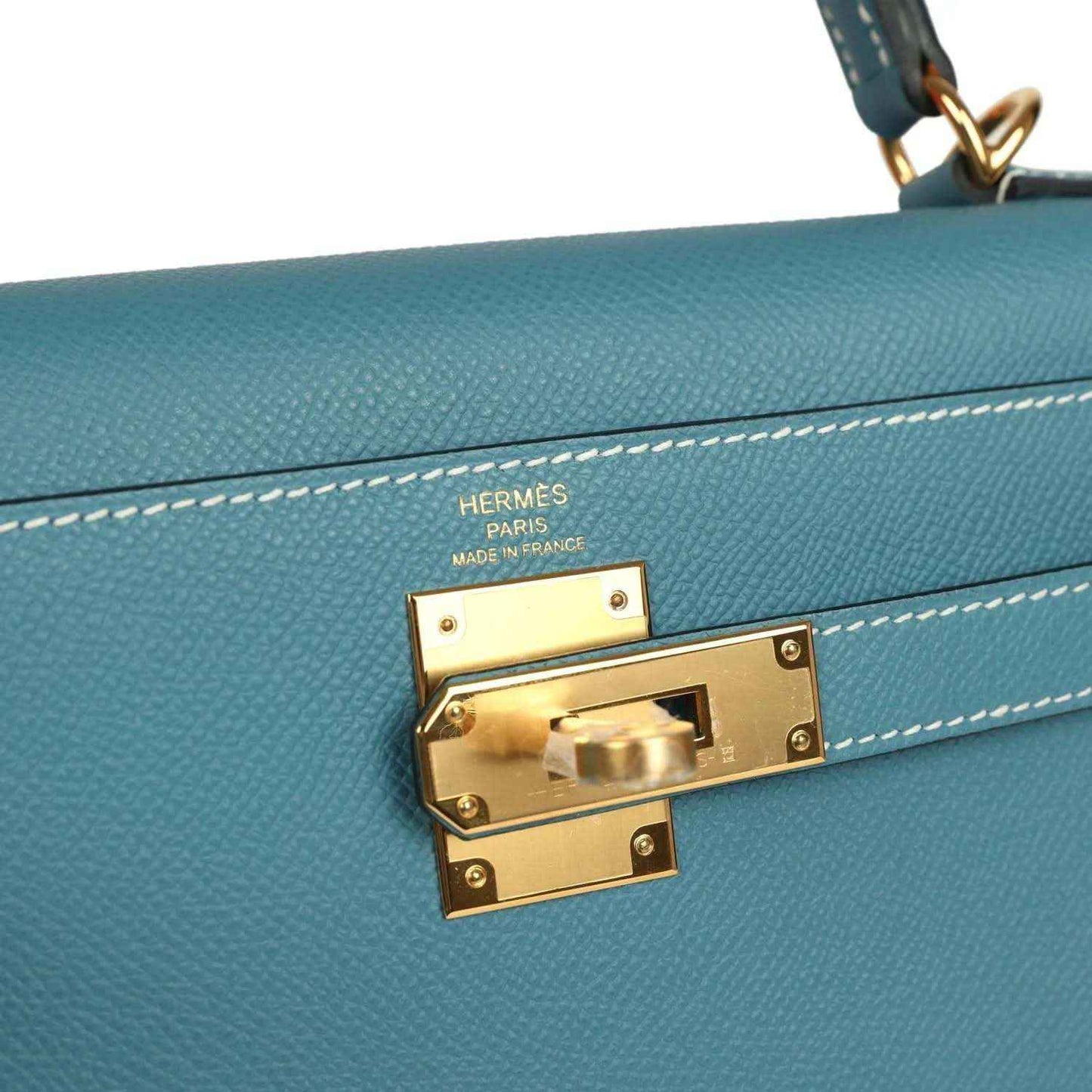 Hermes gold lock hardware on blue leather Kelly bag with engraved brand markings.