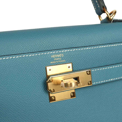 Hermes gold lock hardware on blue leather Kelly bag with engraved brand markings.