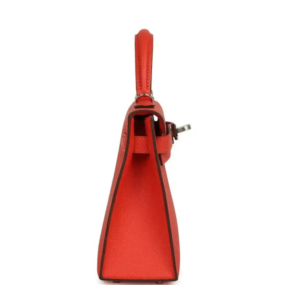 Red mini Kelly bag side view with top handle and leather shoulder strap