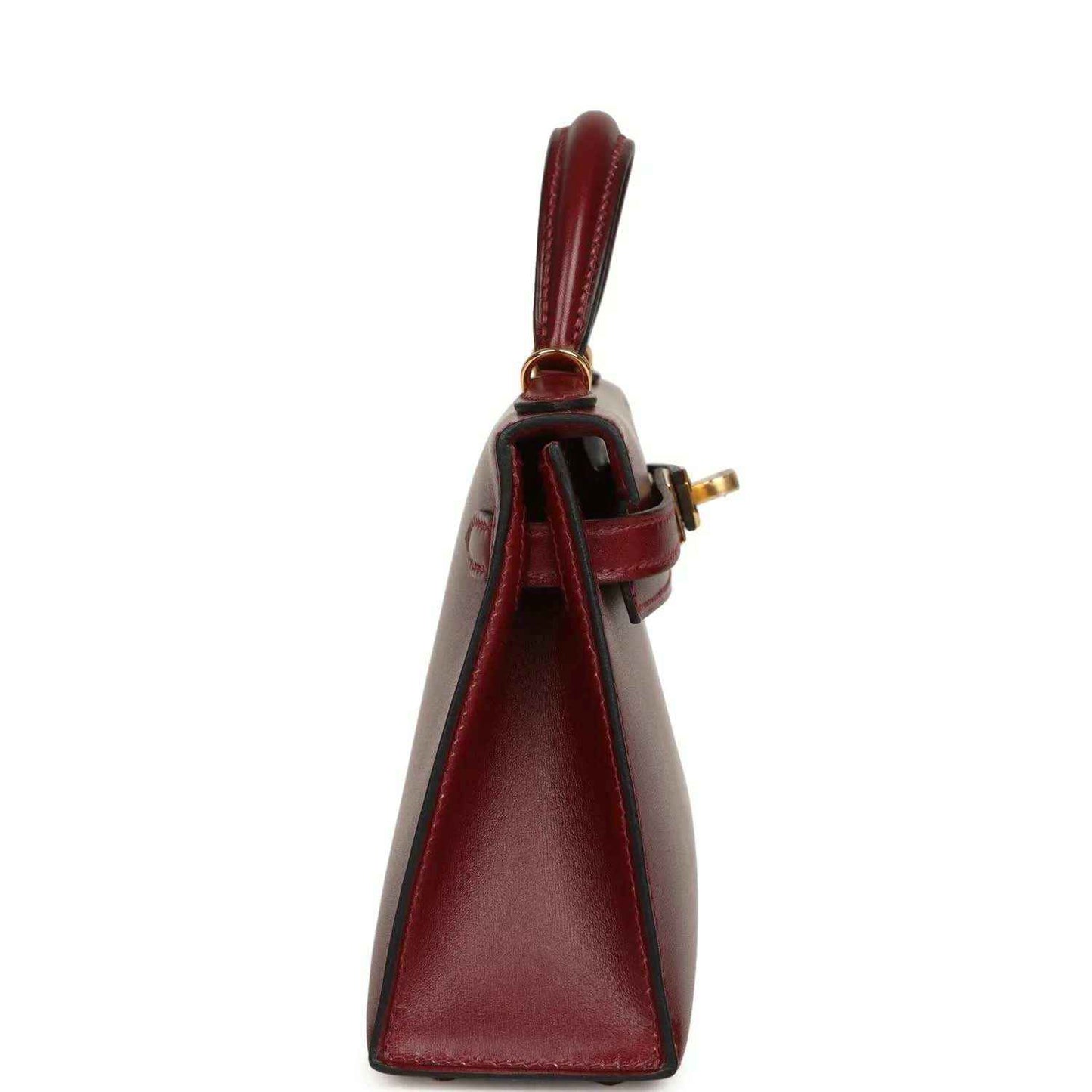Red leather handbag side view with top handle, foldover seam, and gold clasp.