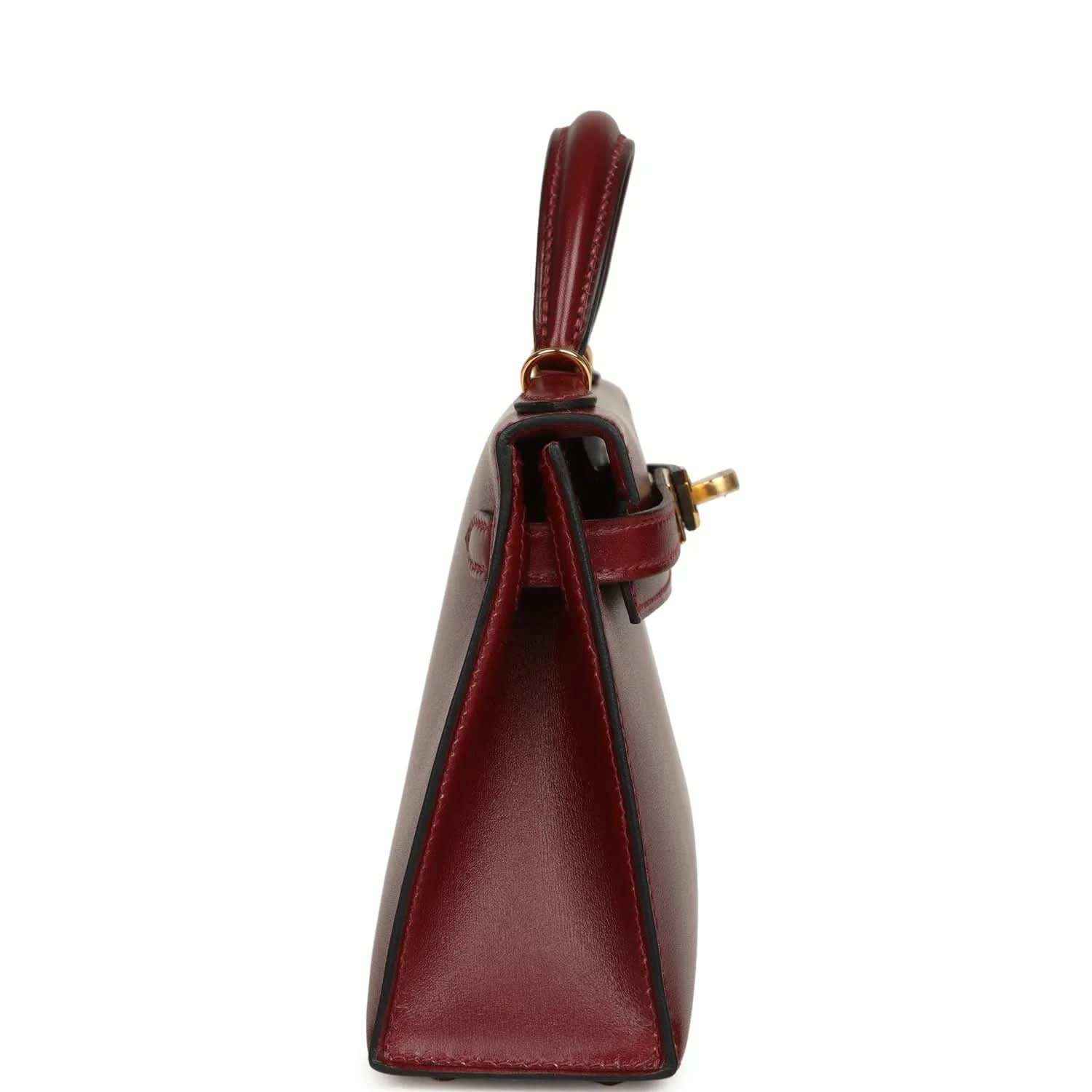 Red leather handbag side view with top handle, foldover seam, and gold clasp.