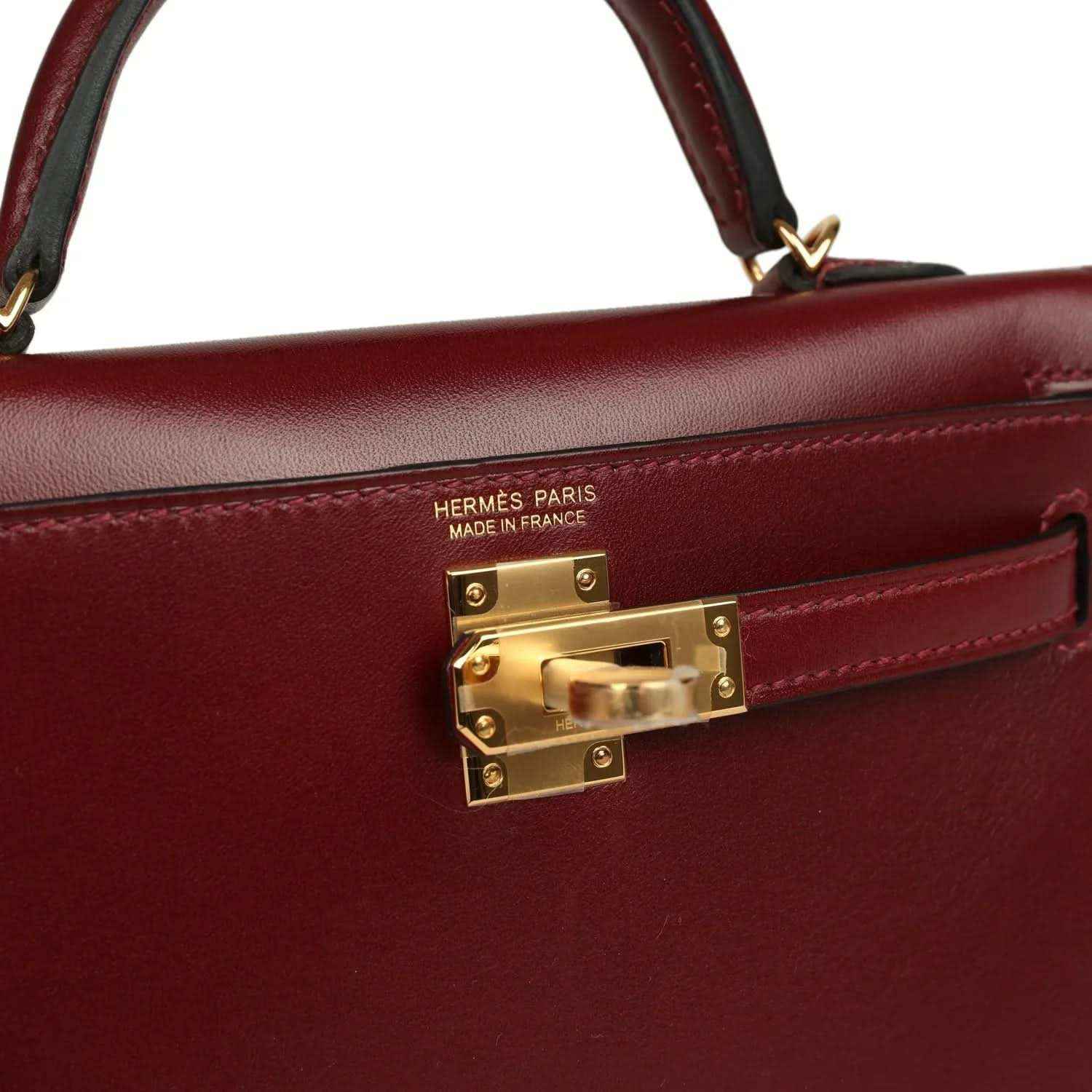 Red leather handbag close-up with Hermès Paris stamp and gold lock hardware.