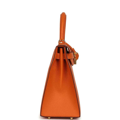 Orange leather Kelly bag with top handle and hanging strap hardware, side view.