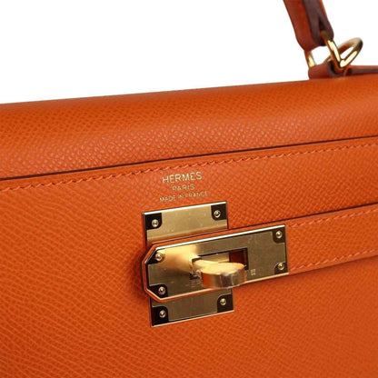 Orange leather Kelly bag with Hermes stamp and gold turn-lock hardware close-up.