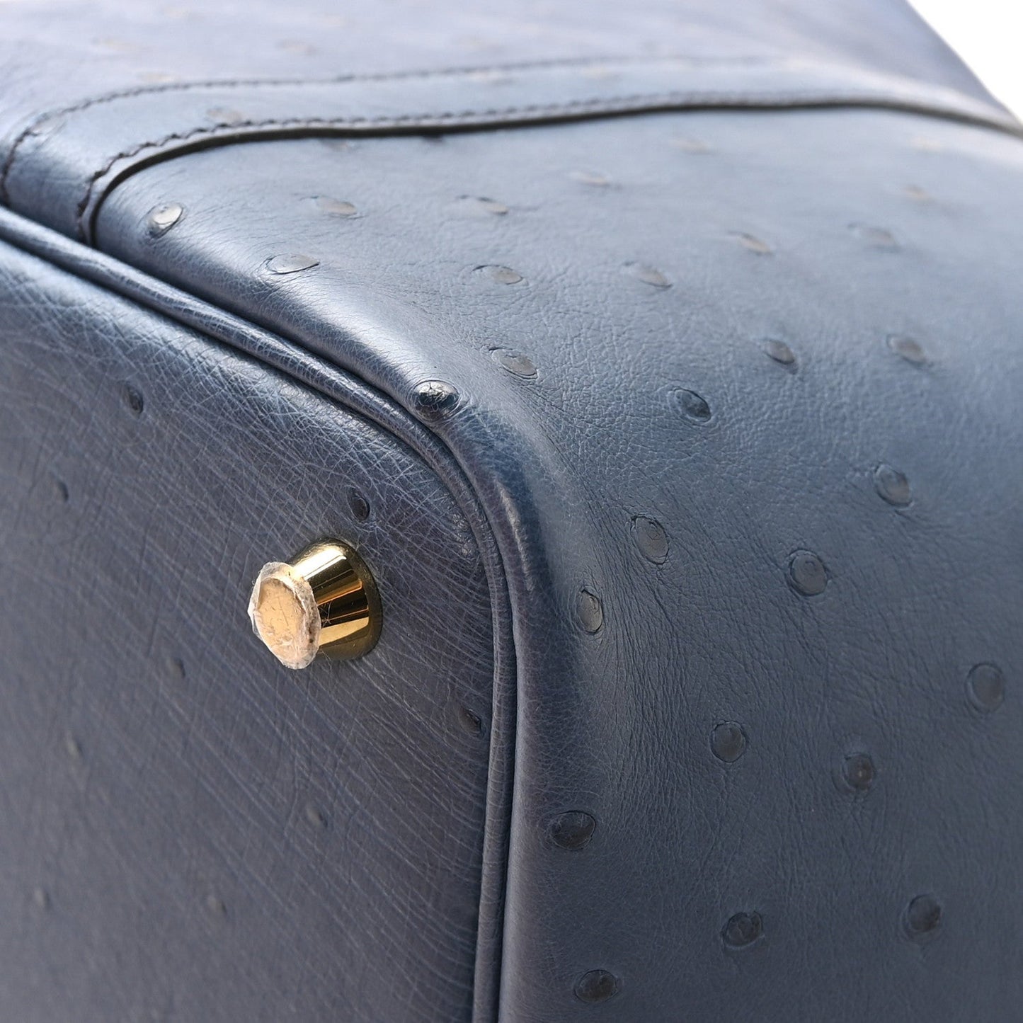Blue ostrich leather bag corner with gold-tone clasp and curved edge.
