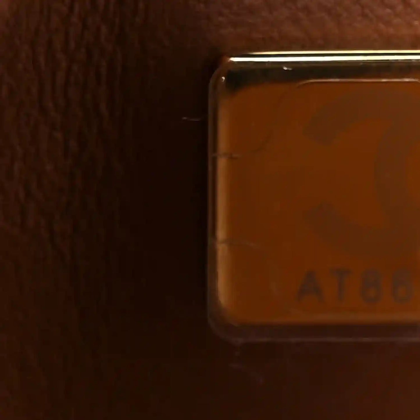 Close-up of brown leather corner edge with hardware and ATELIER marking; smooth trim.