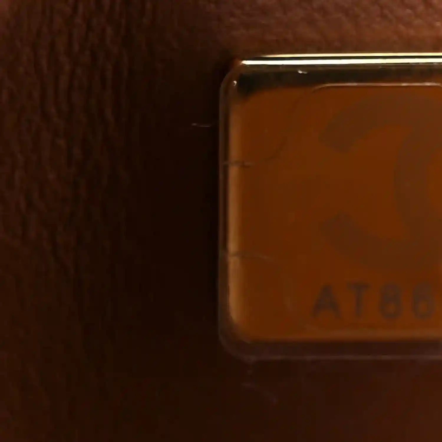 Close-up of brown leather corner edge with hardware and ATELIER marking; smooth trim.