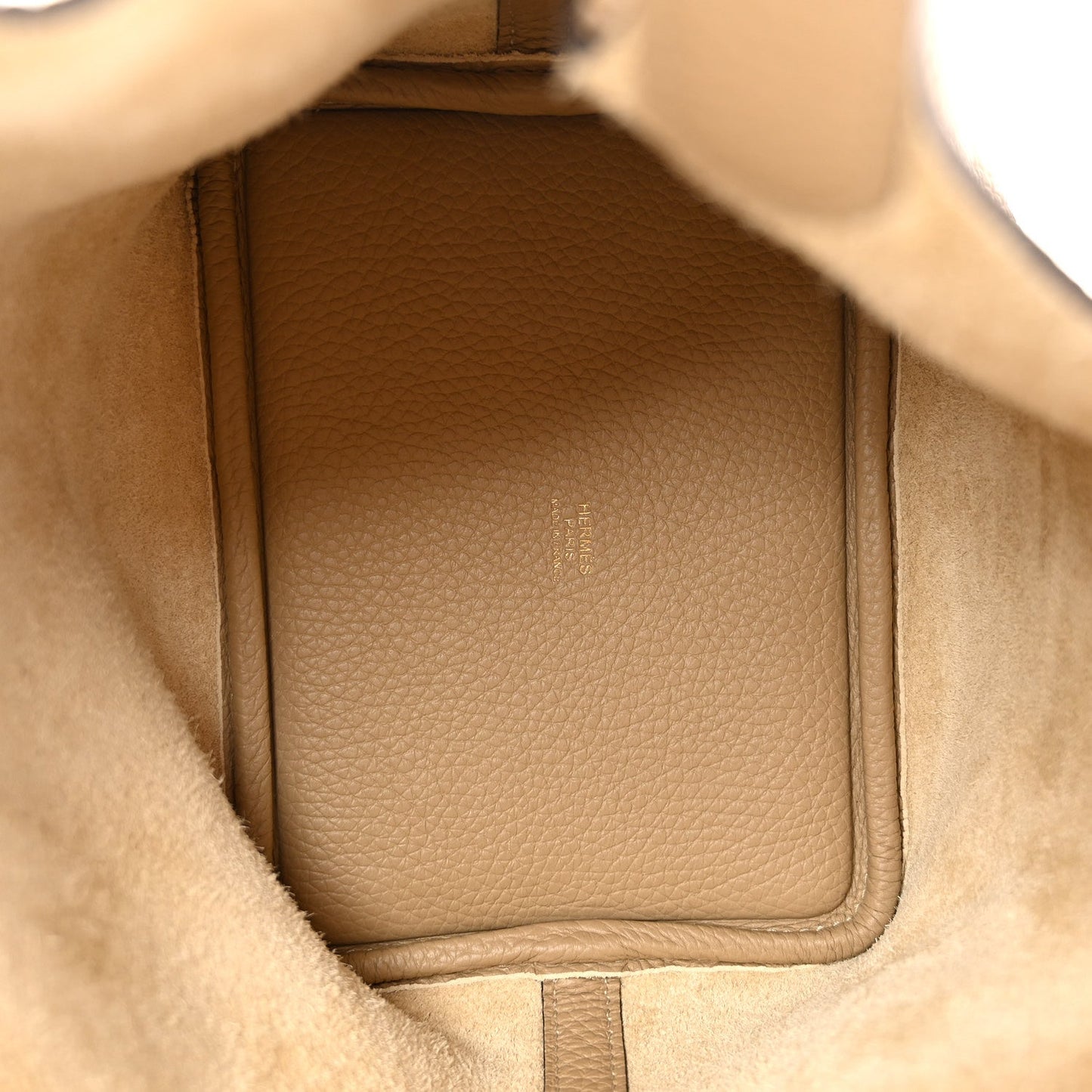 Beige leather bucket handbag interior with structured side panel and seams.