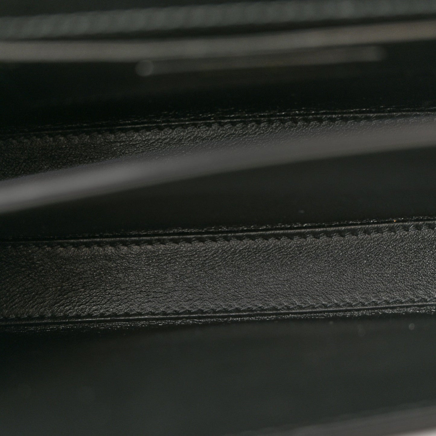 Black leather bag interior seam and textured lining detail.