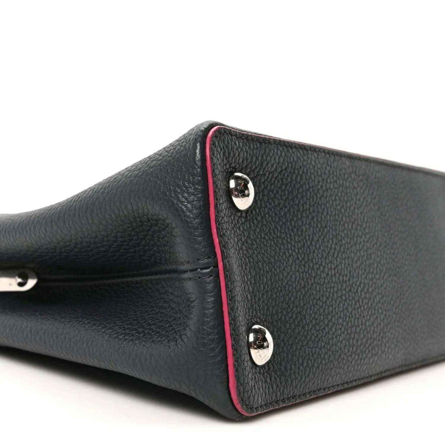 Louis Vuitton Capucines PM leather bag end panel close-up, dark blue with fuchsia piping and studs
