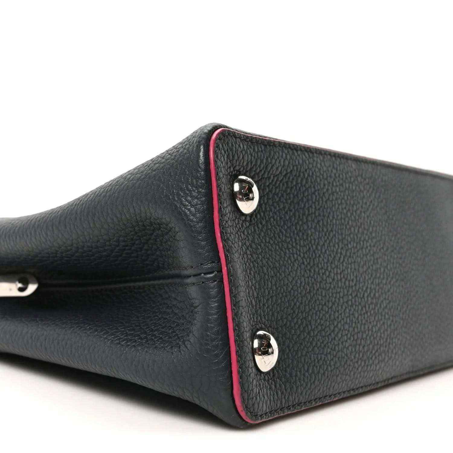 Louis Vuitton Capucines PM leather bag end panel close-up, dark blue with fuchsia piping and studs