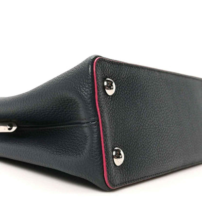 Louis Vuitton Capucines PM leather bag end panel close-up, dark blue with fuchsia piping and studs