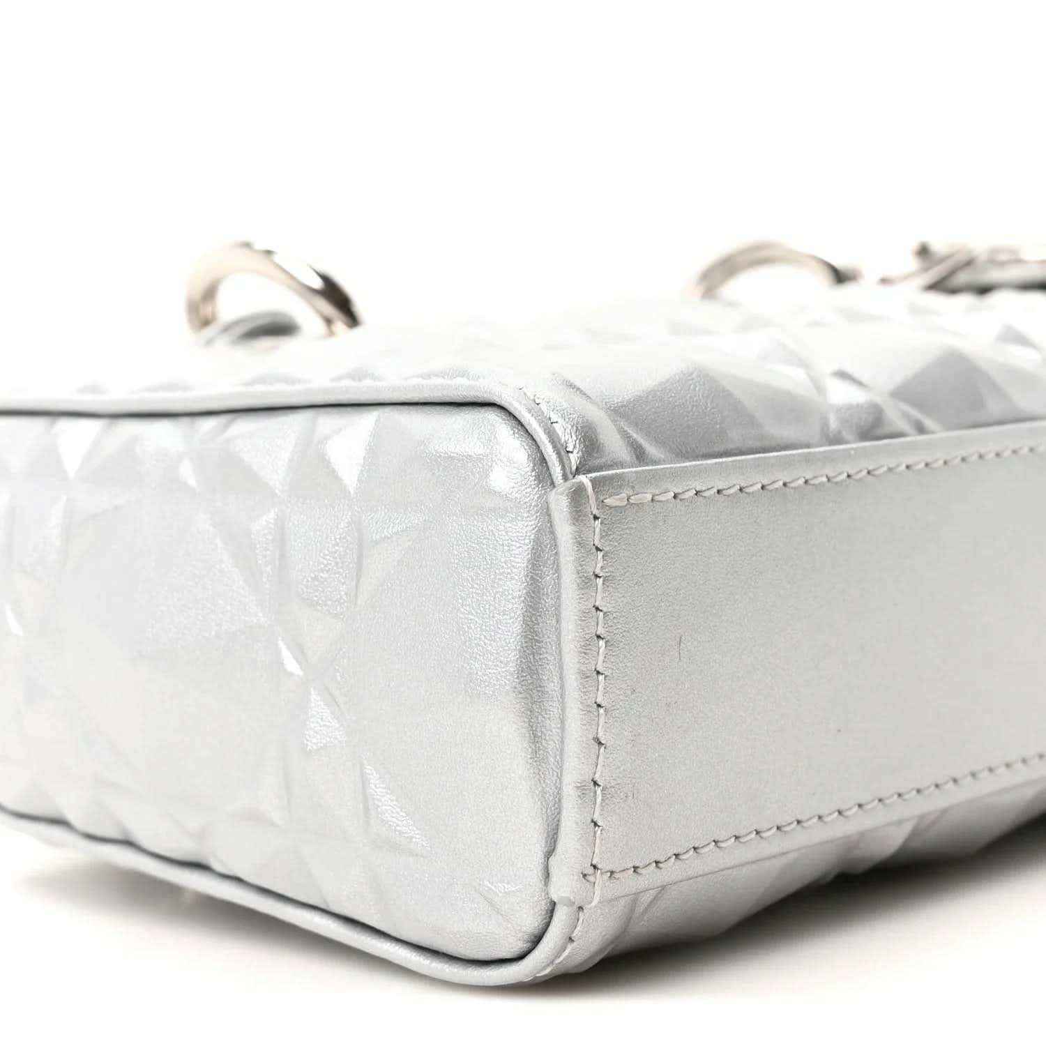 Small metallic silver handbag side panel with geometric texture and stitched edge.