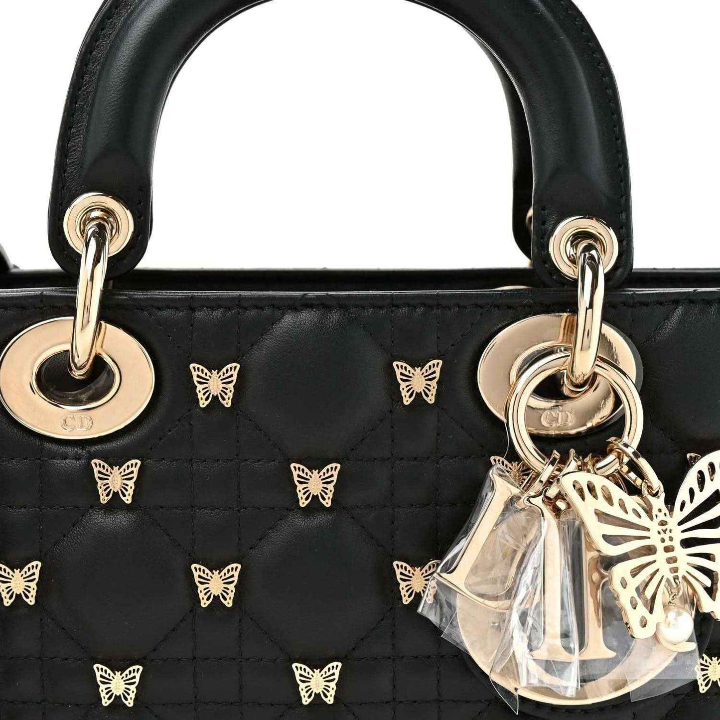 Black quilted handbag with top handles, butterfly charms, and gold Dior-style letter charm