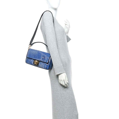 Blue denim baguette bag with black strap and gold hardware; worn over shoulder