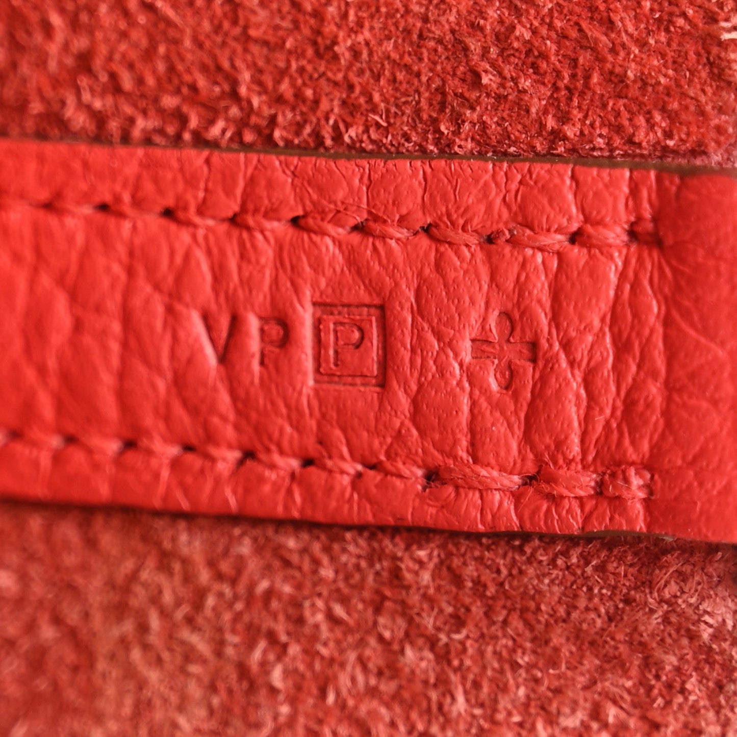 Red leather strap label with stitched border and embossed emblem