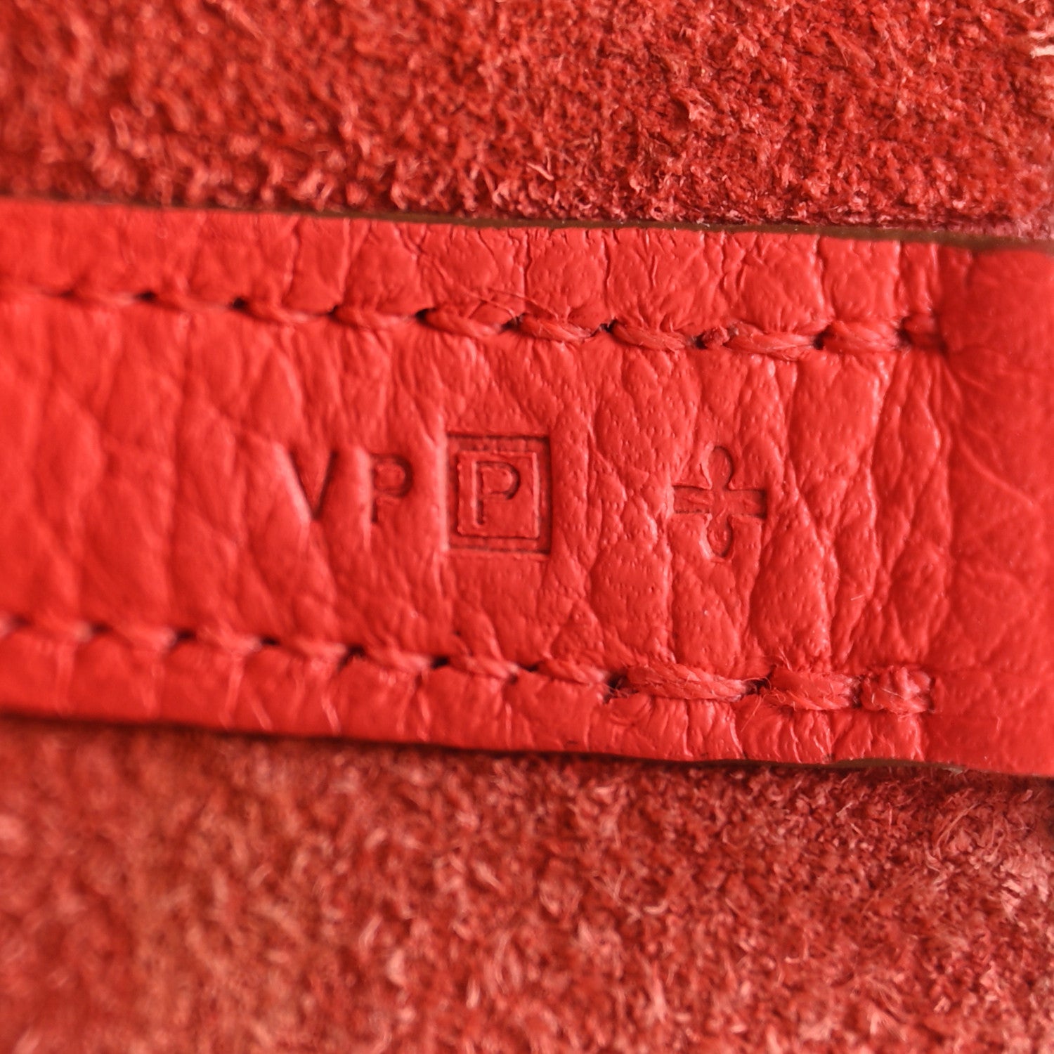 Red leather strap label with stitched border and embossed emblem