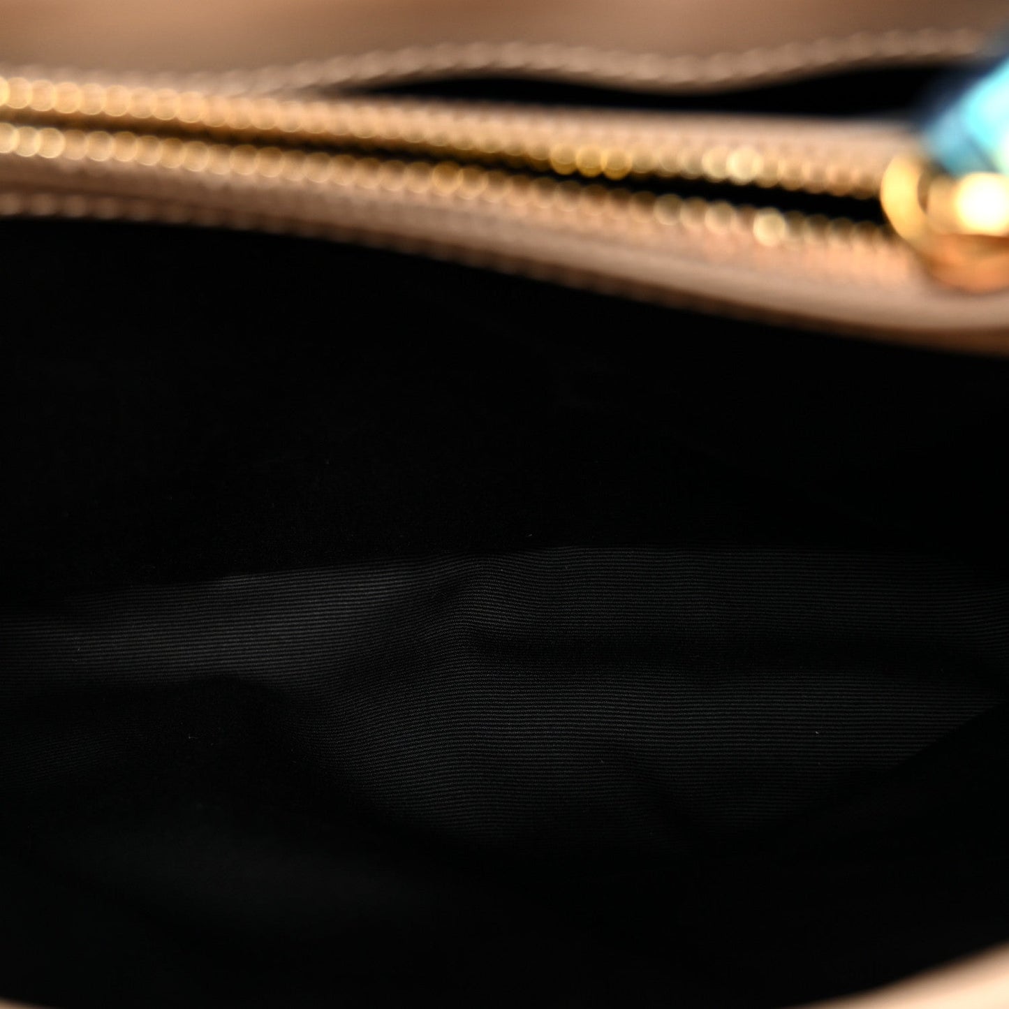 Satchel interior lining close-up with dark fabric and gold chain hardware edge