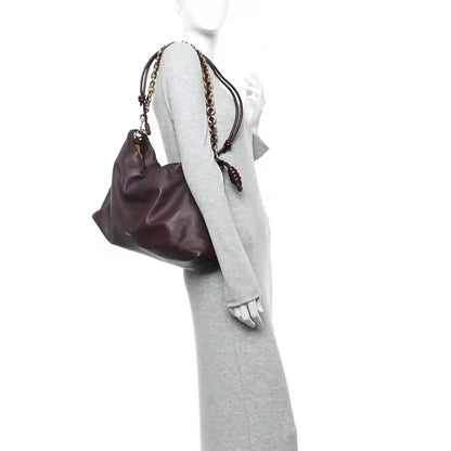 Dark burgundy leather clutch worn on mannequin with gold chain strap