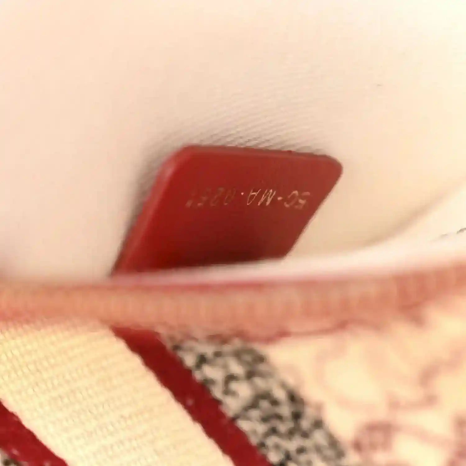 Red leather tag detail on canvas bag, partially visible lettering.
