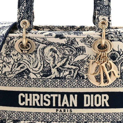 Blue toile de Jouy handbag close-up with gold rings, tassel charm, and “CHRISTIAN DIOR” text.