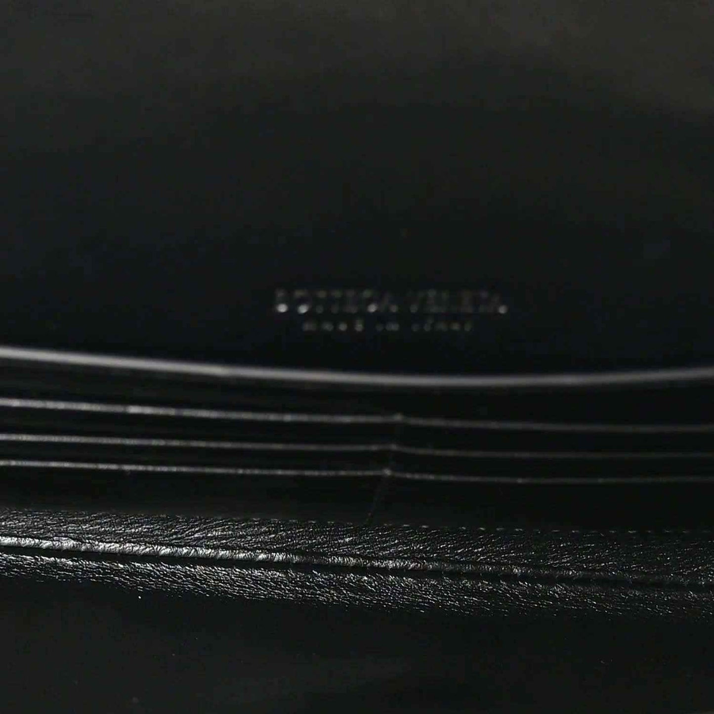 Black leather clutch flap detail with subtle stitching and hardware