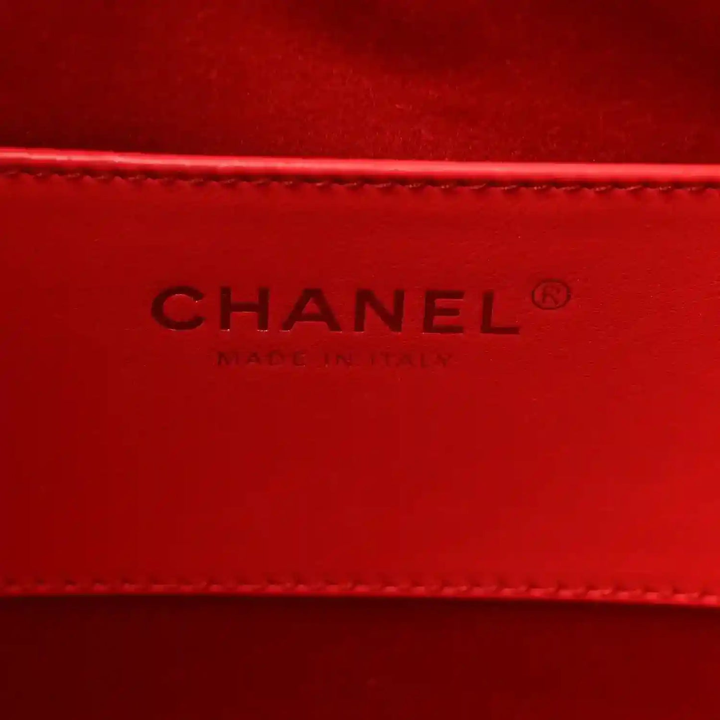 CHANEL leather logo on burgundy interior panel with stitched edge.