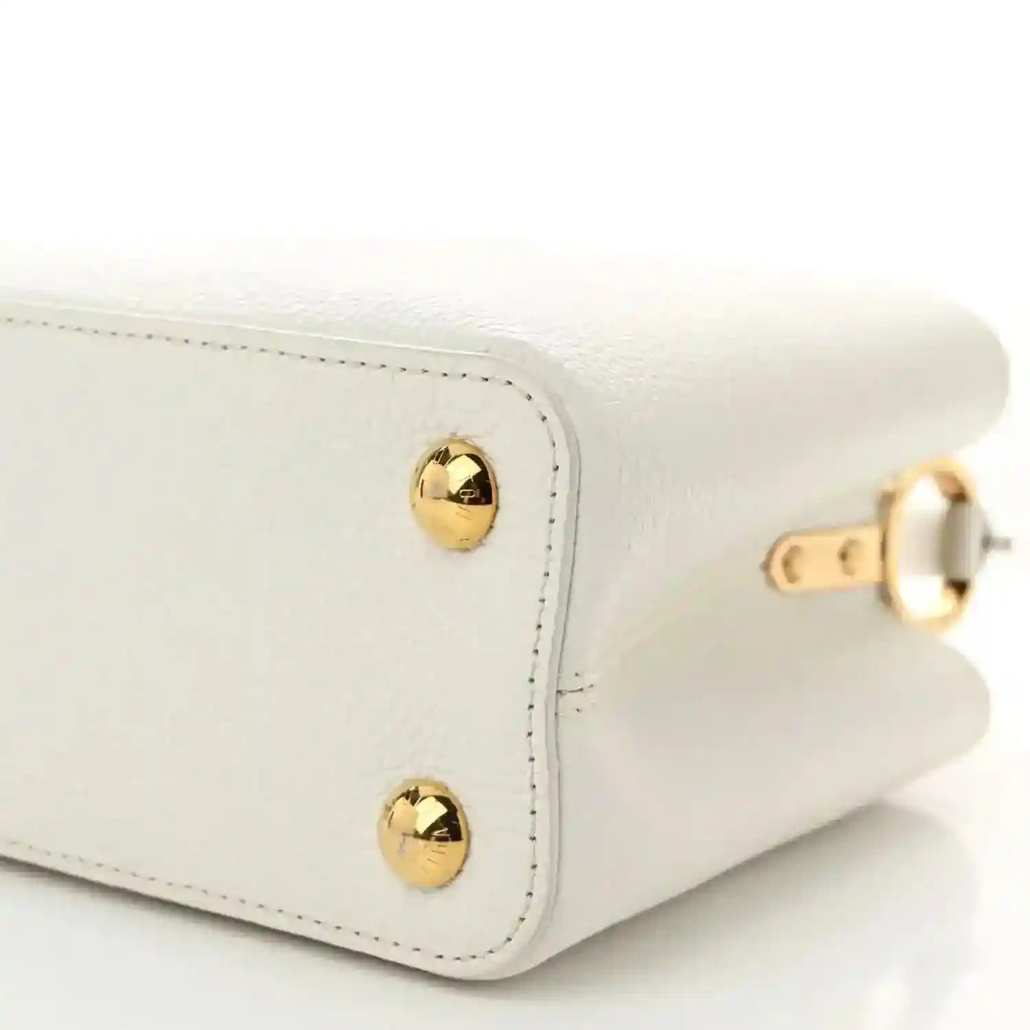 White small top-handle bag corner with gold stud hardware and stitched seam