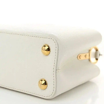 White small top-handle bag corner with gold stud hardware and stitched seam