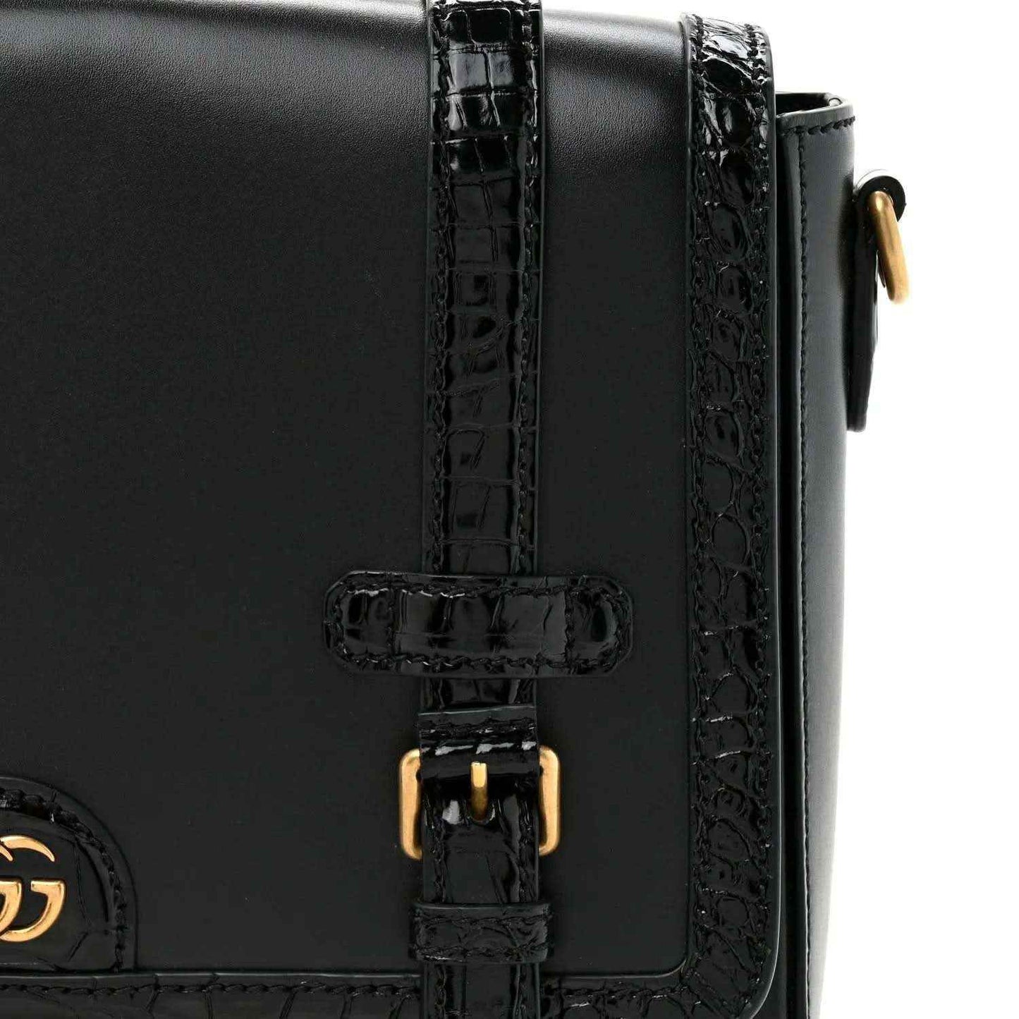 Black leather messenger bag close-up of double buckle with gold-toned hardware