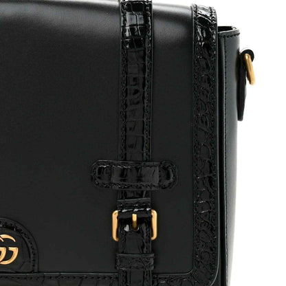 Black leather messenger bag close-up of double buckle with gold-toned hardware