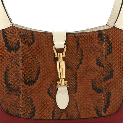 Snakeskin hobo bag top clasp with gold hardware and cream strap attachments.