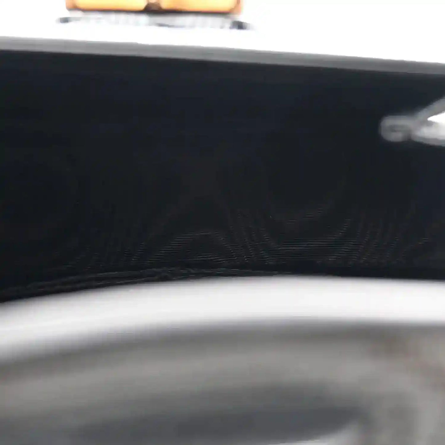 Close-up of black bag front with embossed pattern and curved top edge trim