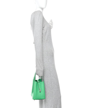 Green leather tote bag with top handles and center zipper lock, on a sleeve