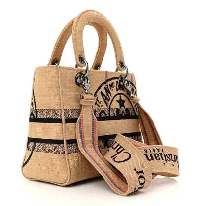 Medium jute canvas tote with top handles, embroidered graphic panels, dangling metal charm.