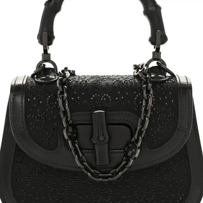 Black mini handbag with bamboo-style handle, chain strap, and front clasp detail.