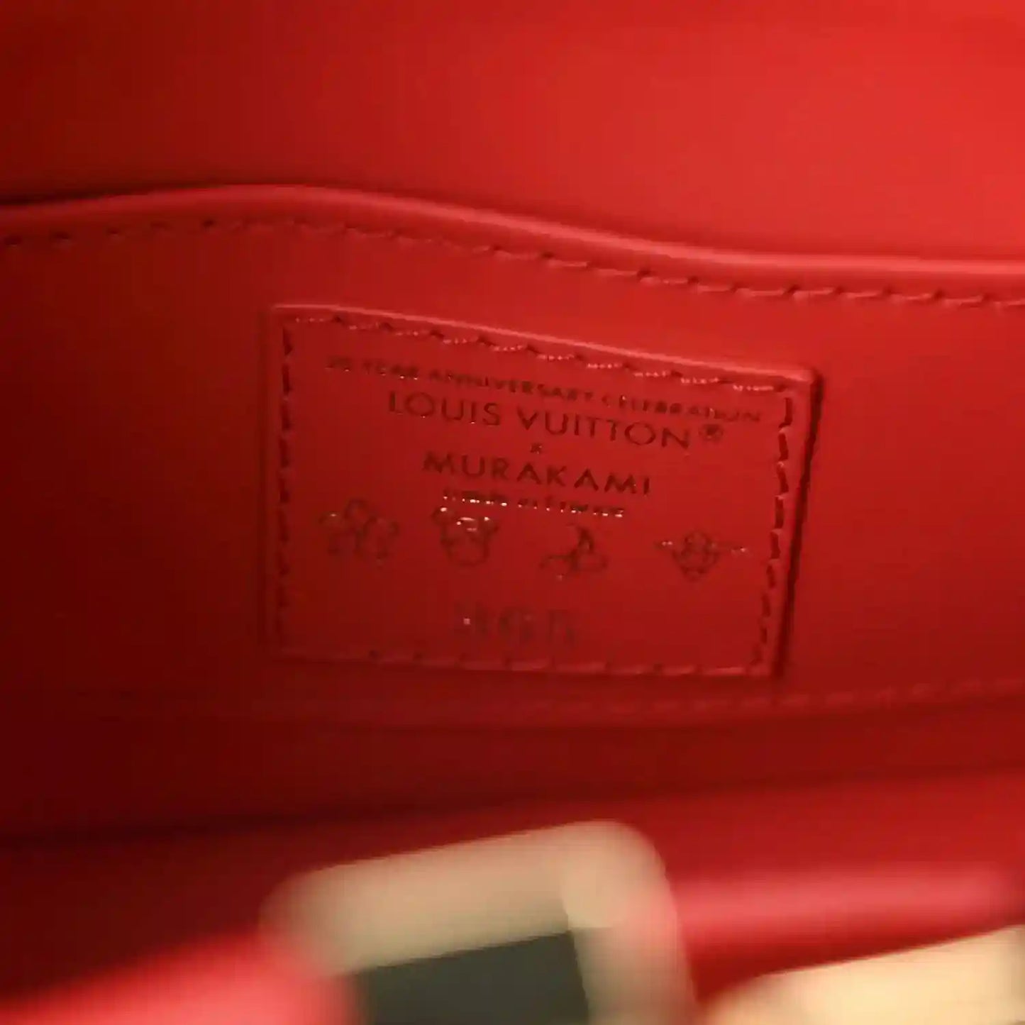 Red leather mini handbag interior label patch with Louis Vuitton and Murakami text.