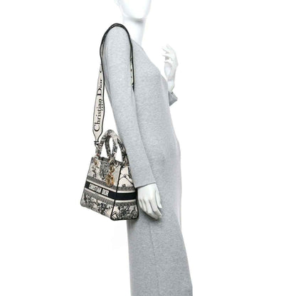 Medium tote handbag with toile print and adjustable shoulder strap, carried at side.