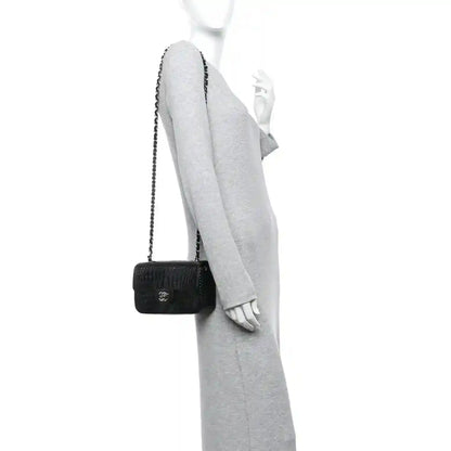 Black mini flap bag with short chain strap, worn crossbody on an arm.