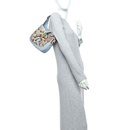Small hobo bag held at side, featuring snakeskin print and light blue leather trim