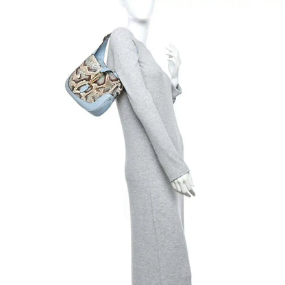 Small hobo bag held at side, featuring snakeskin print and light blue leather trim