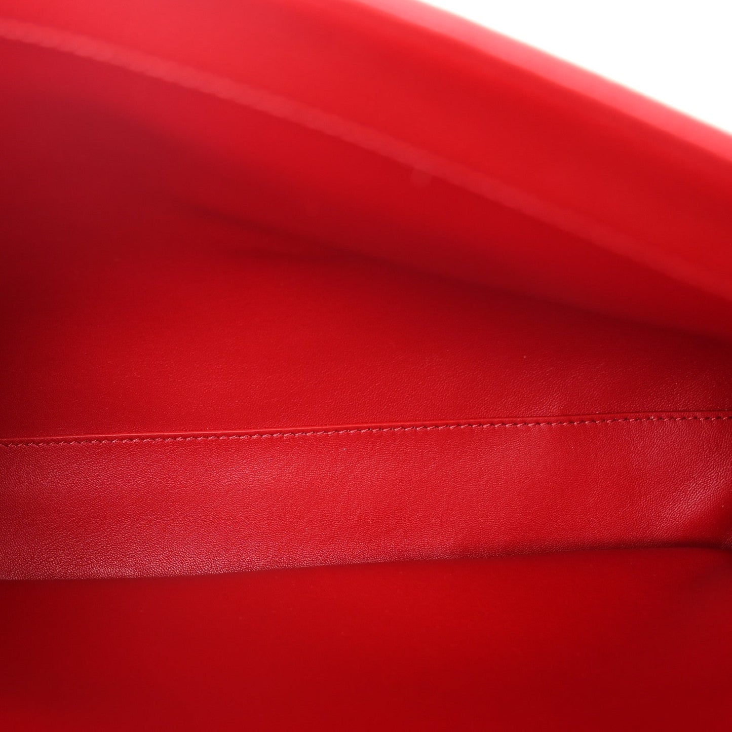 Close-up of red grained leather with contrast stitching along the bag edge