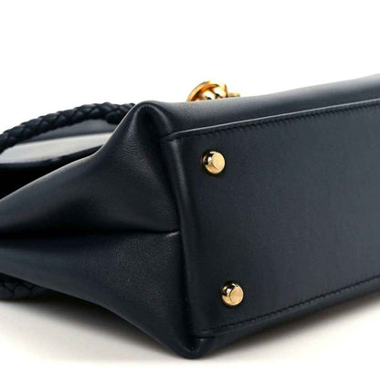 Black small handbag with gold-tone corner studs and braided strap opening