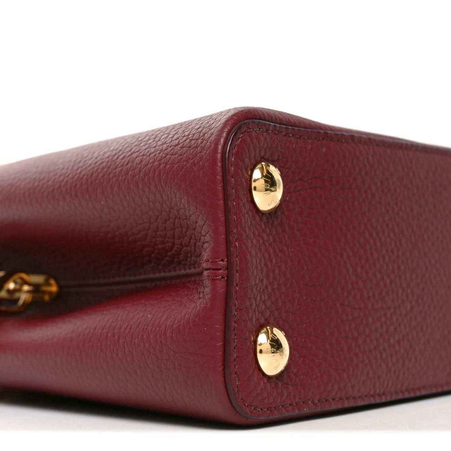 Bordeaux leather handbag corner with textured grain and two gold snap studs.