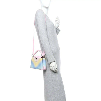 Mini Capucines bag worn crossbody, rainbow leather with pink strap and metal clasp