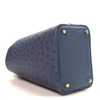 Blue ostrich leather bucket bag with gold corner hardware and turn-lock closure.