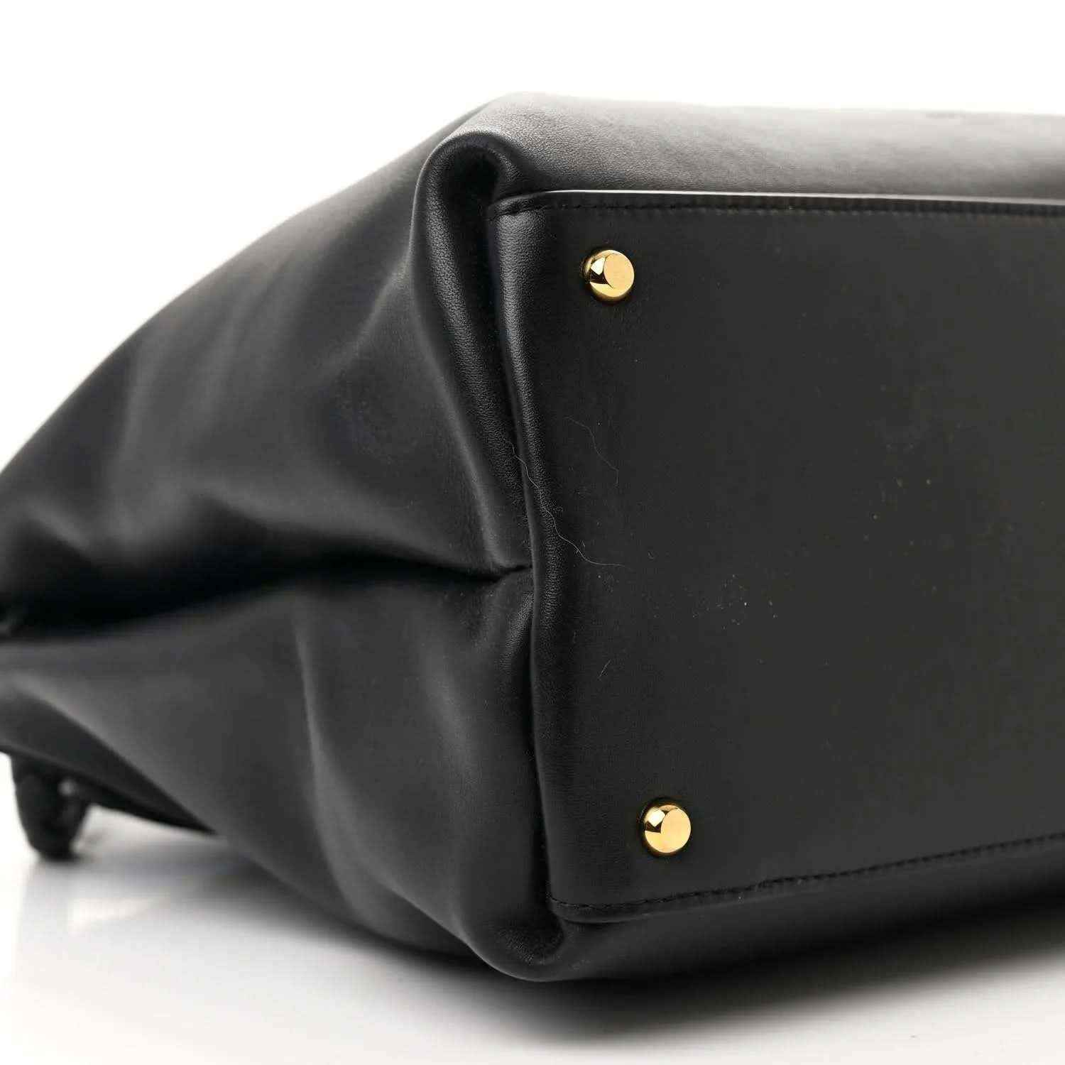 Black leather shoulder bag corner with gold round studs and stitched trim.