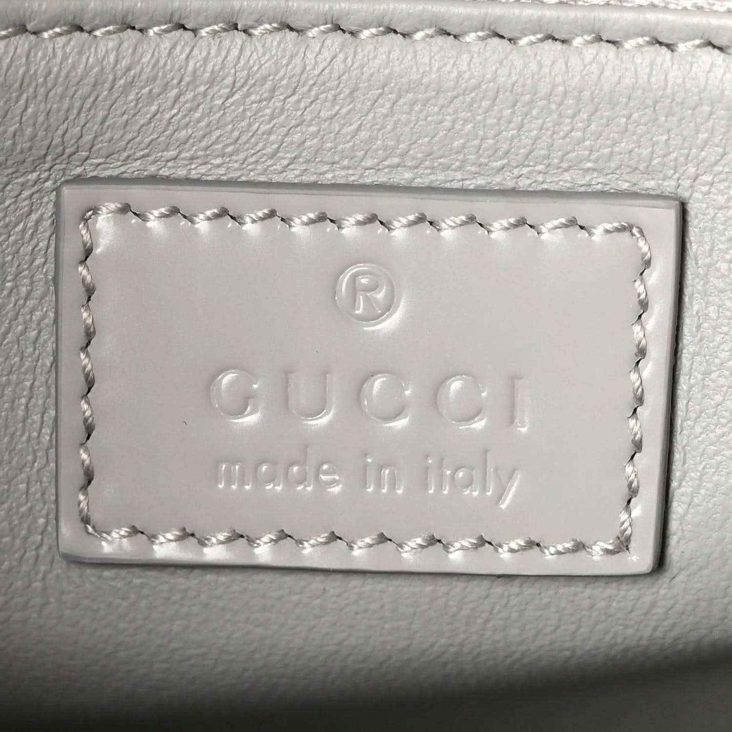 Light grey leather bag label with embossed Gucci and “Made in Italy” text