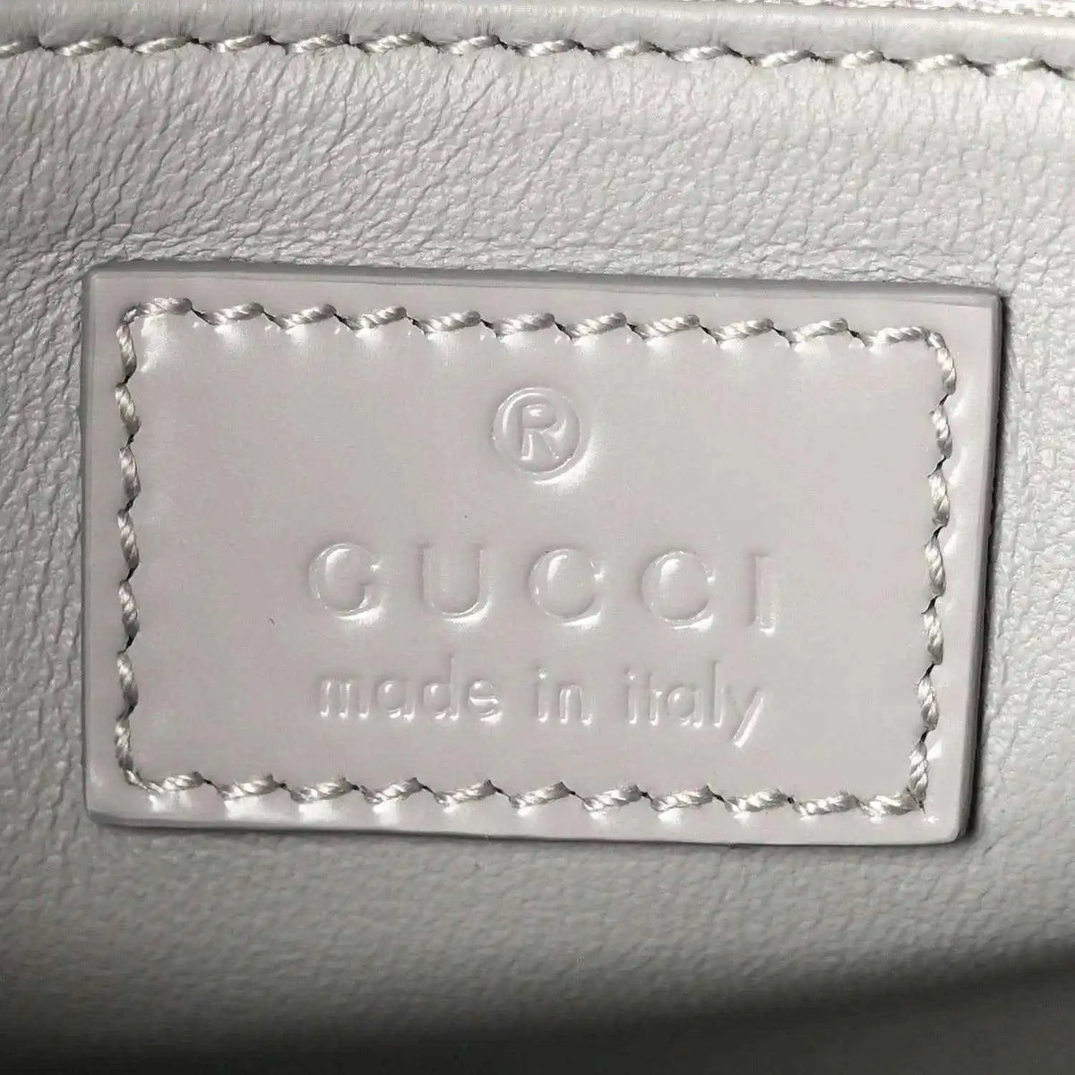 Light grey leather bag label with embossed Gucci and “Made in Italy” text