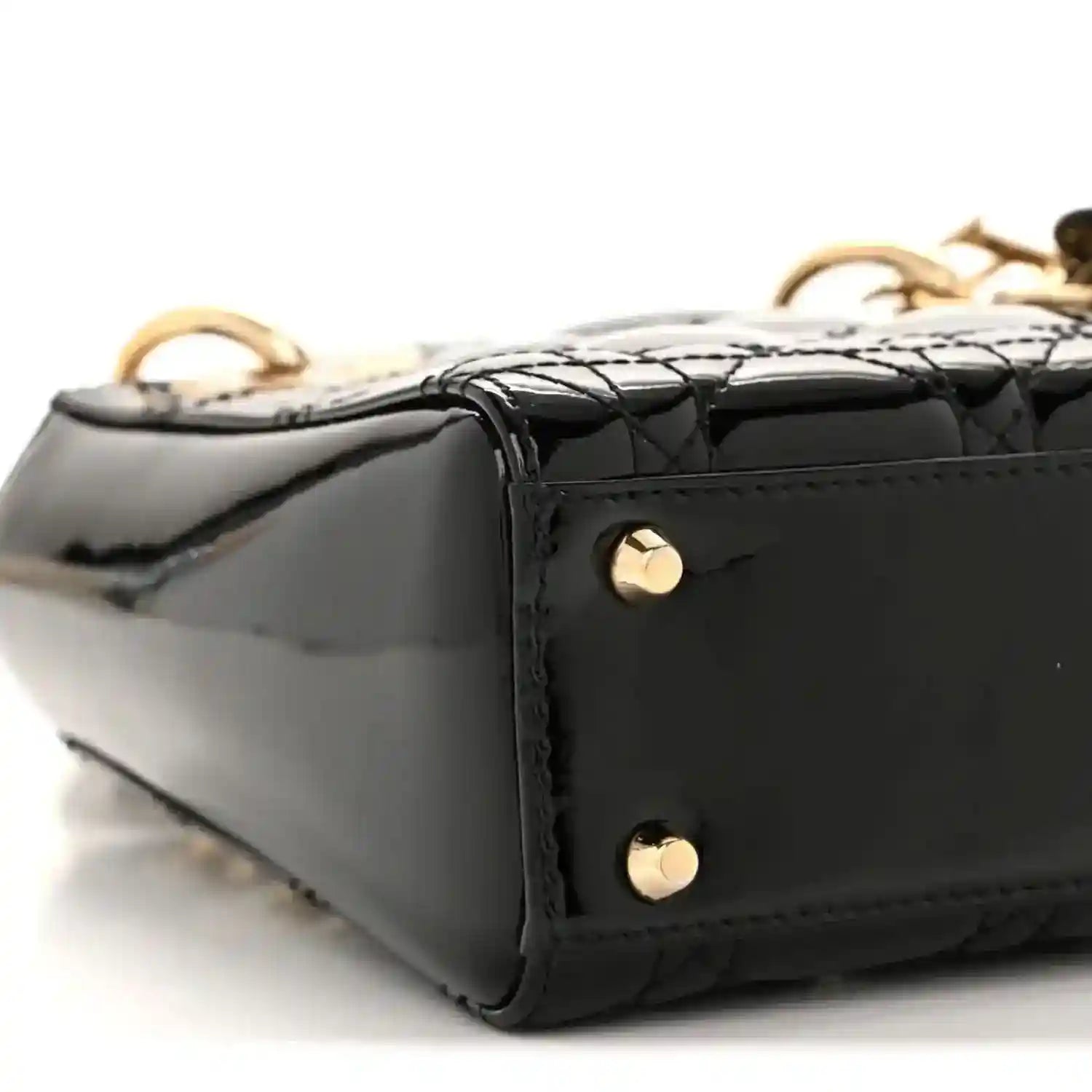 Black patent mini handbag bottom corner with gold rivet feet and quilted edge detail
